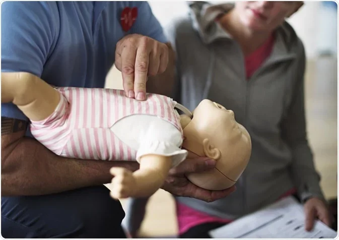 Two people practicing CPR on a baby mannequin during a training session.