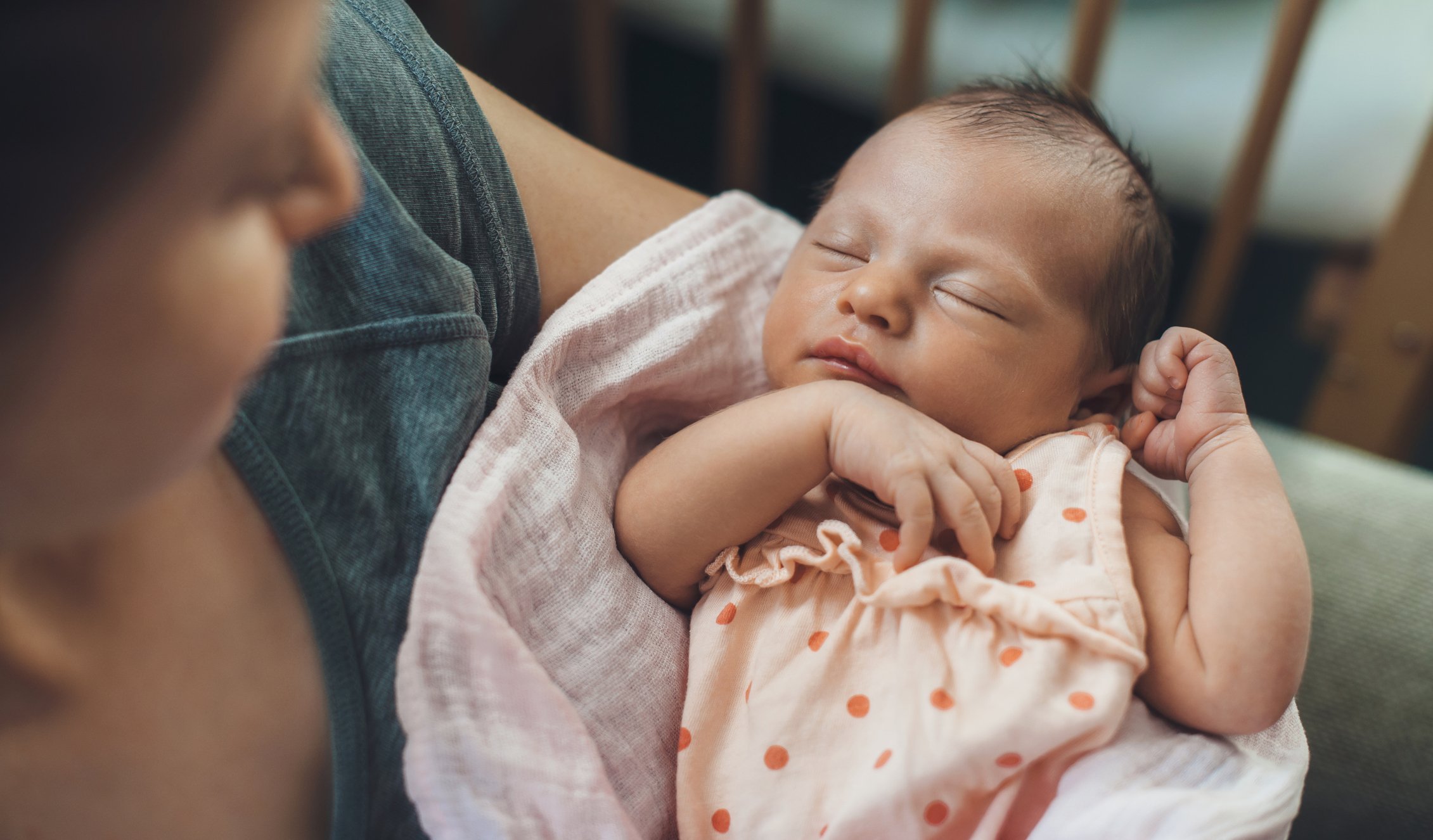A baby sleeping peacefully in someone's arms, with the baby's eyes closed and hand near its face.