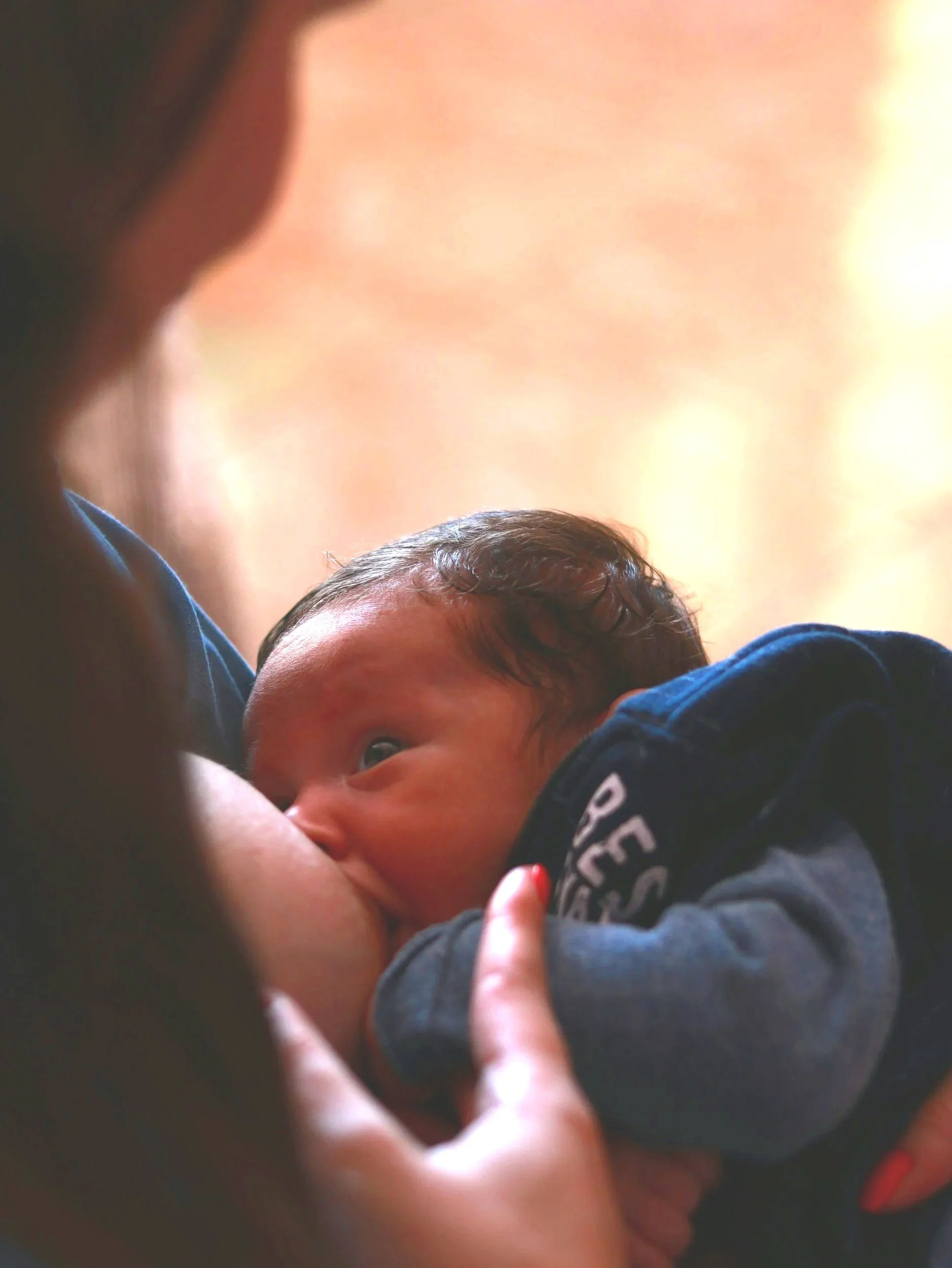 Close-up of a baby breastfeeding, with the mother holding the baby and supporting its head.