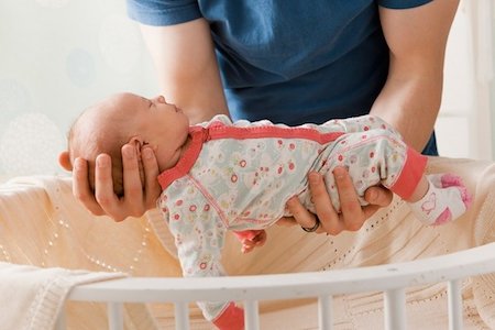 Person holding a newborn baby above a crib.