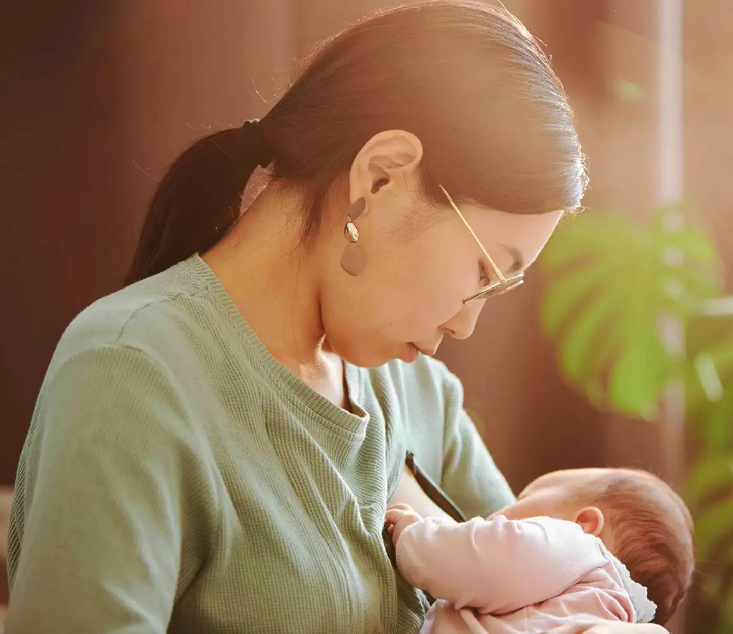 A woman breastfeeding a baby in a hospital bed, with a nurse assisting and monitoring.