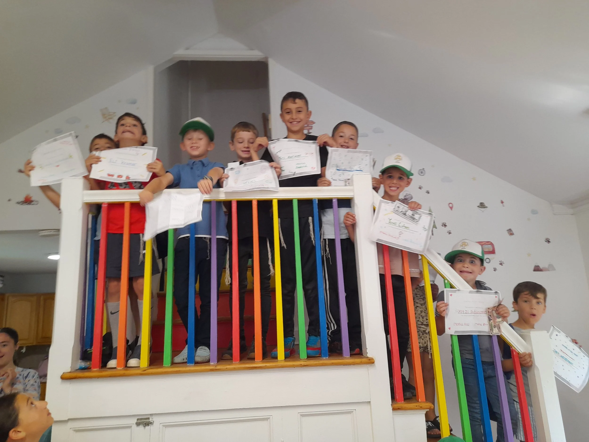 Children standing on a colorful lofted platform holding certificates and smiling.