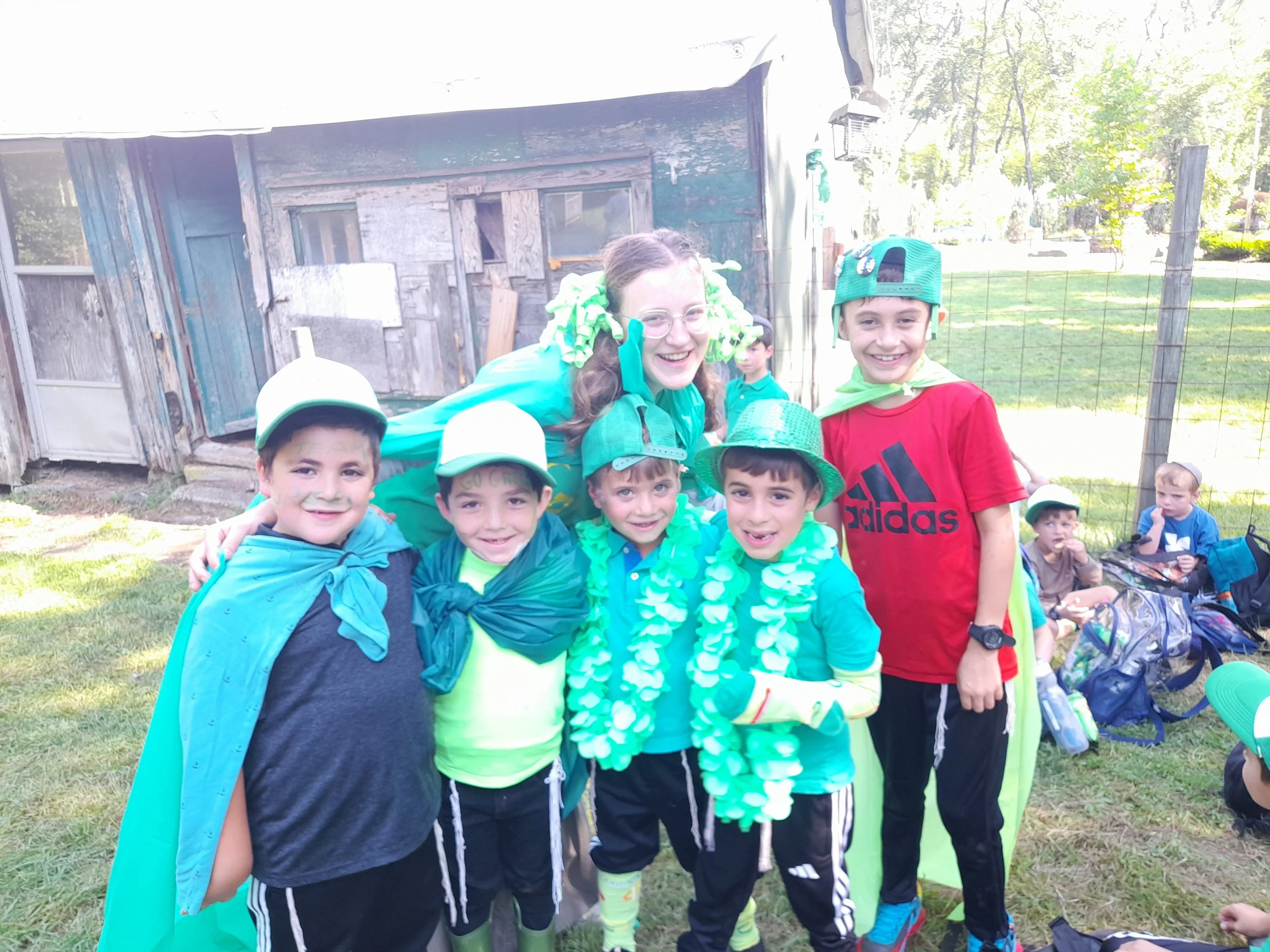 Group of children and an adult dressed in green costumes for a festive outdoor event, smiling for a photo.