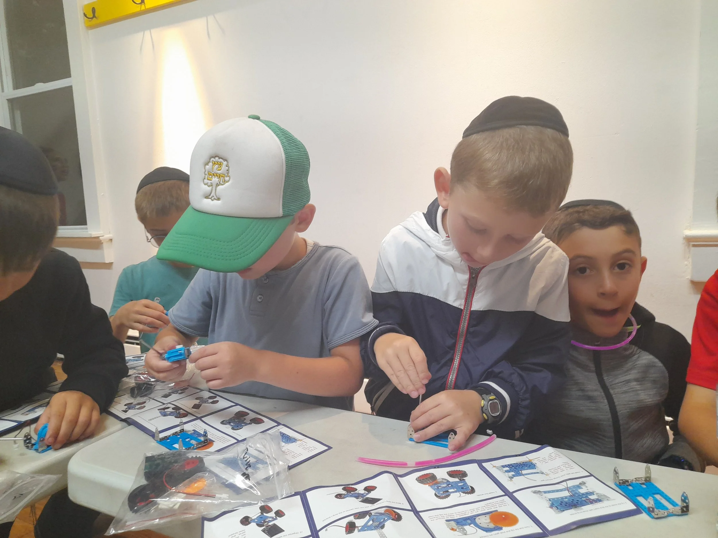 Group of children assembling robot kits at a table, with instruction manuals and robot parts.