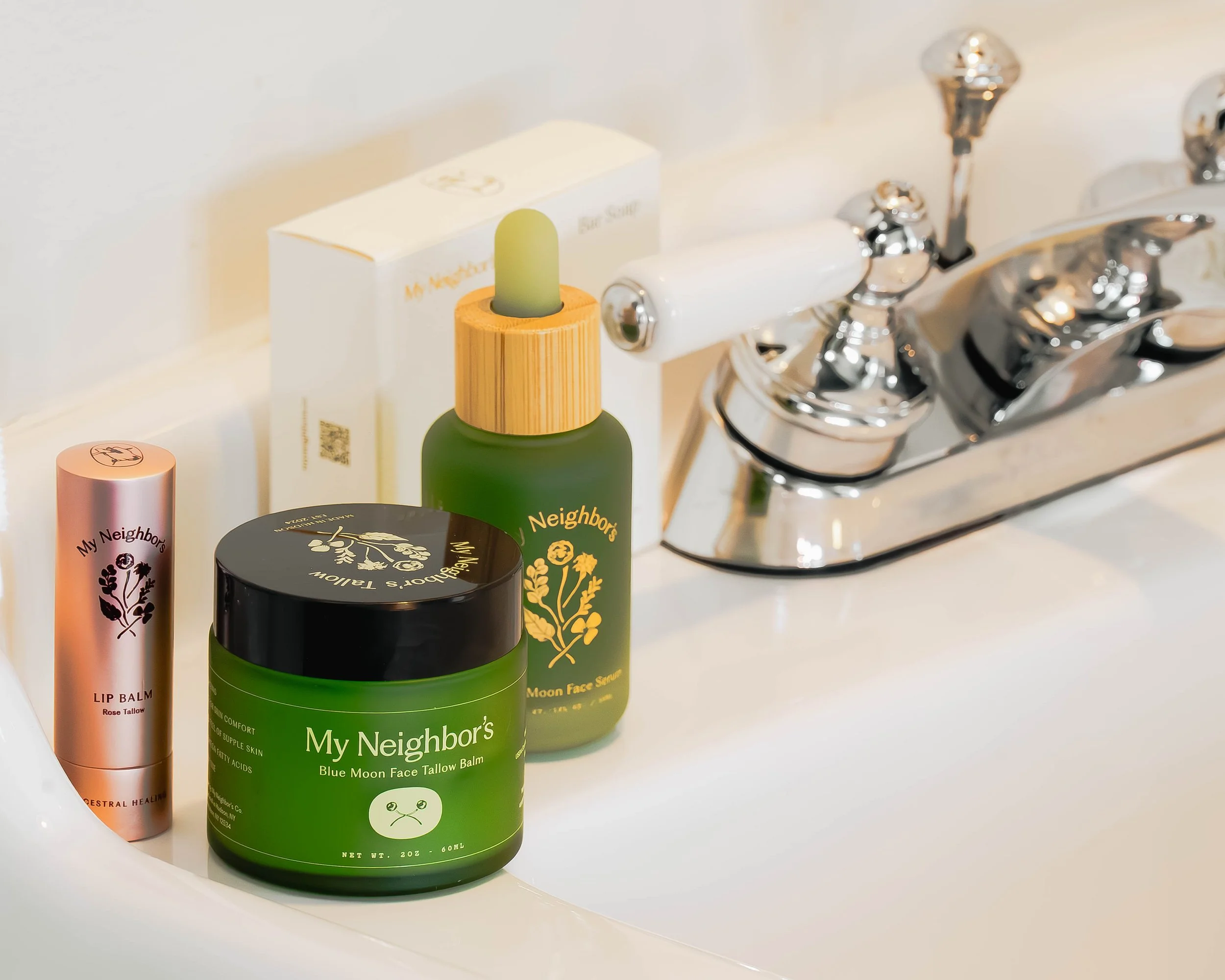 Array of skincare and beauty products on a white bathroom counter, including lip balm, face balm, and face serum bottles.