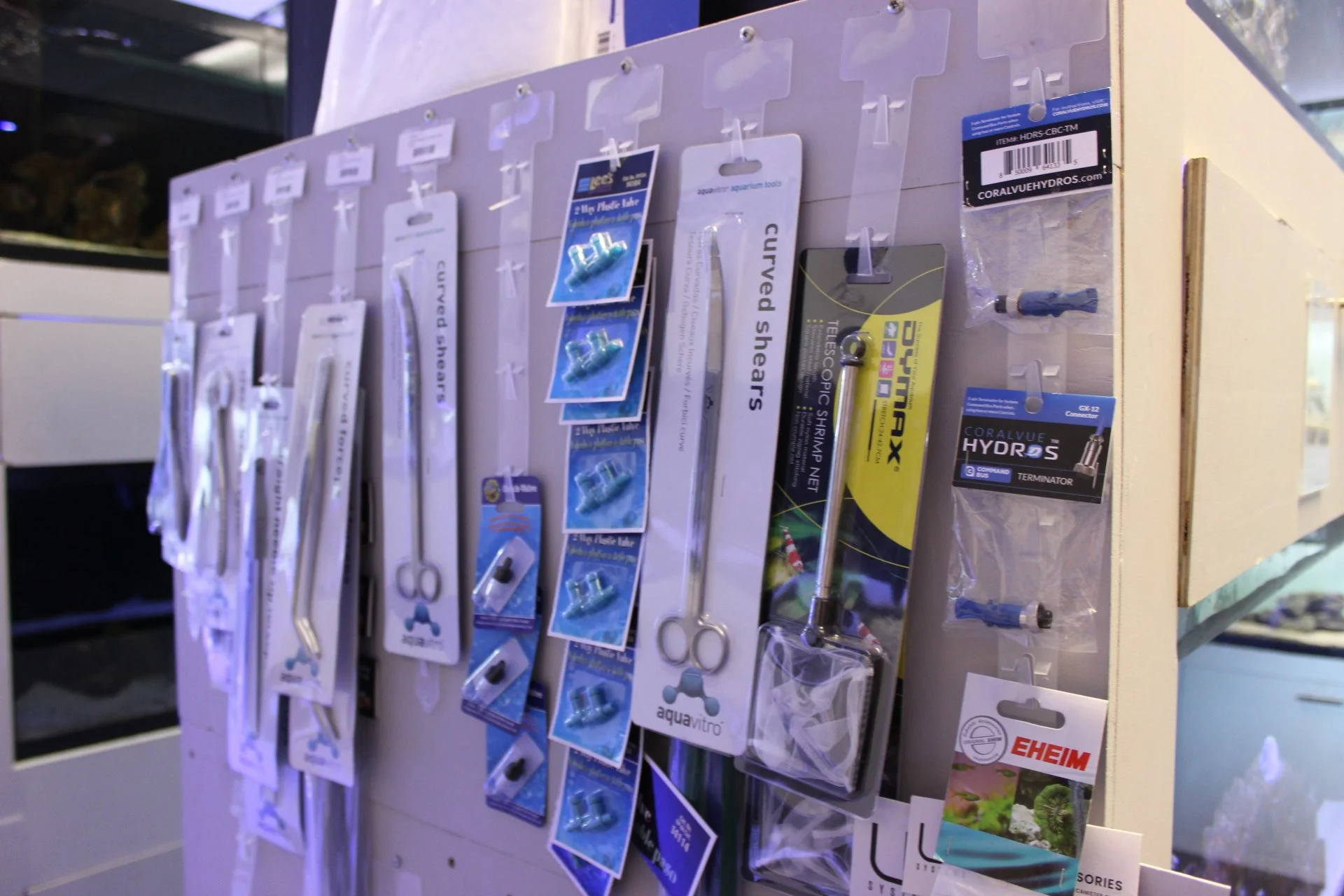 Display of various aquariums supplies, including curved shars, tubing, connectors, and small tools, hanging on a white board at a store.