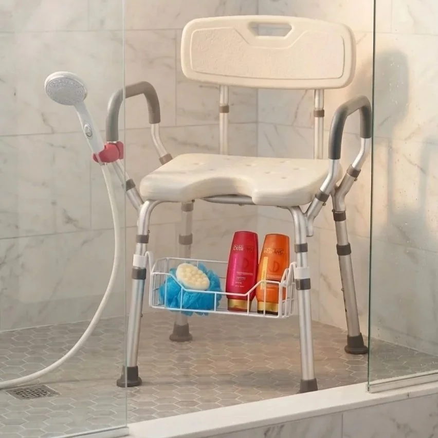 Image shows a shower chair sitting in a shower.  It has an attachment to hold the handheld shower head, as well as a basket under the shower chair for holding soap and other bathroom necessities