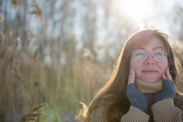 woman with face in hands in a field and at peace