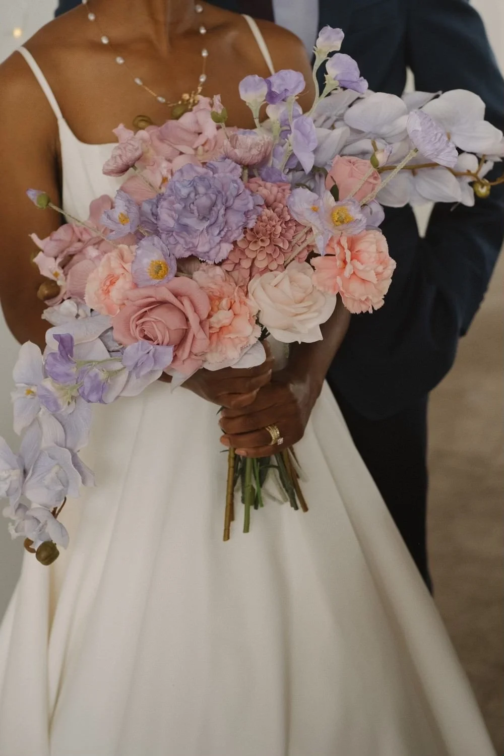 A bride holds a purple and pink bridal bouquet made of faux wedding flowers rented from JayBird Events