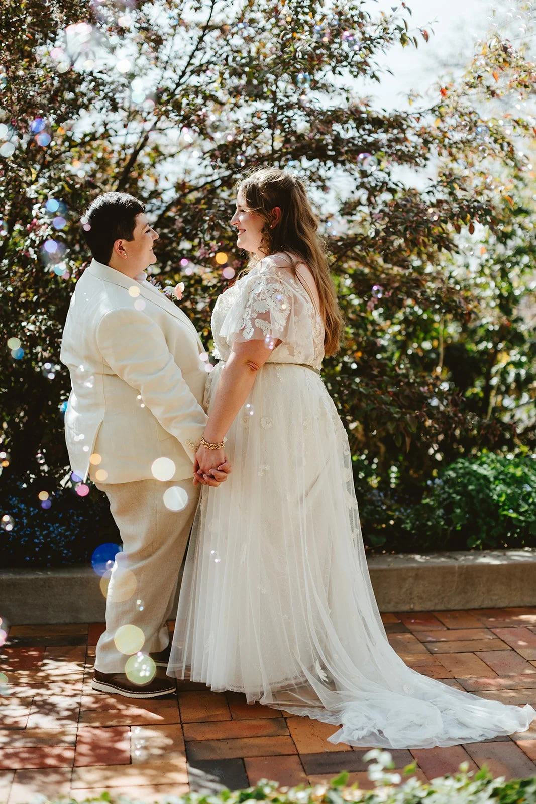 Bubbles float in front of two brides, who are standing together holding hands at their wedding planned by JayBird Weddings and Events.