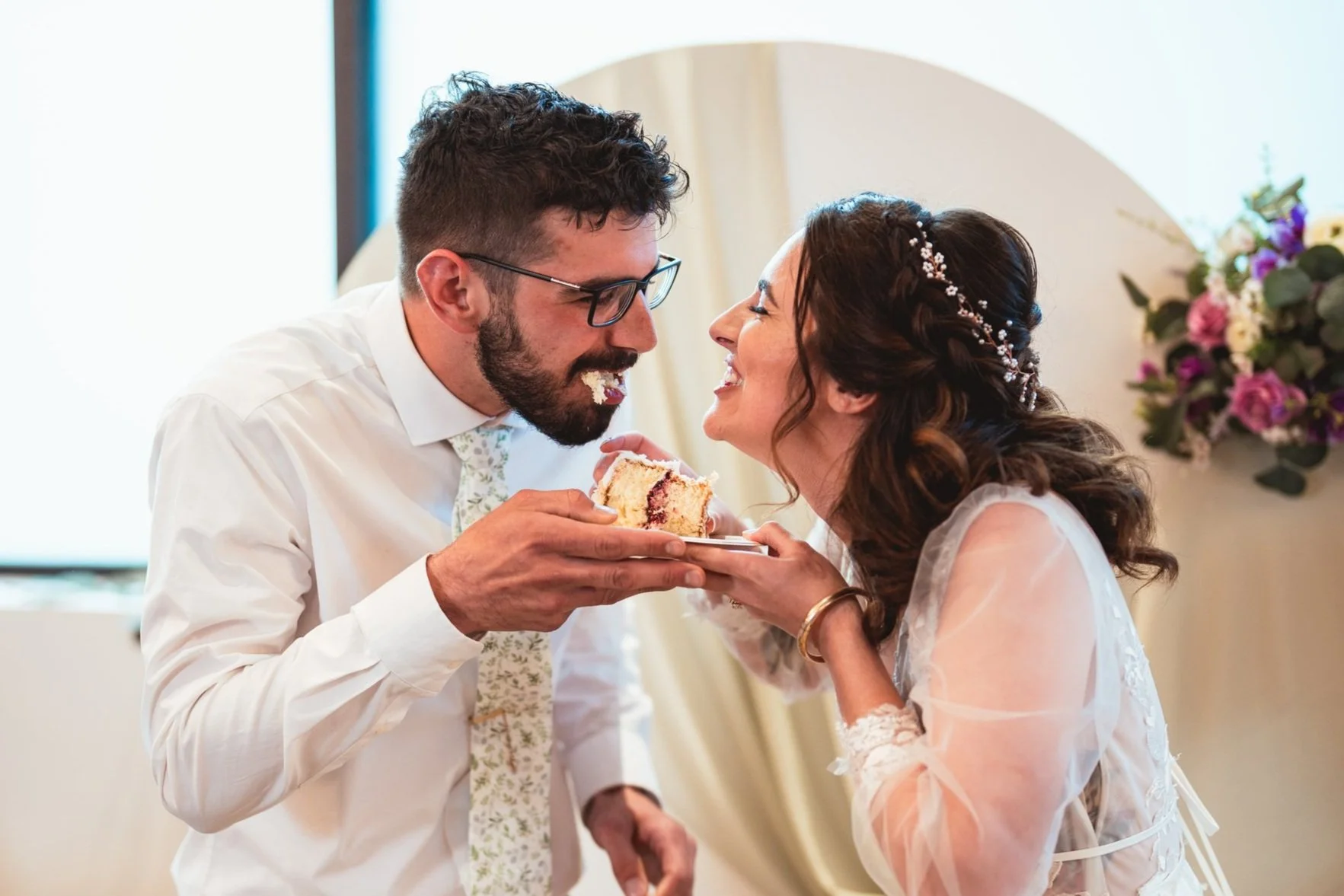 A bride and groom look at each other eating their wedding cake on their wedding day in Denver, Colorado, planned by JayBird Weddings and Events