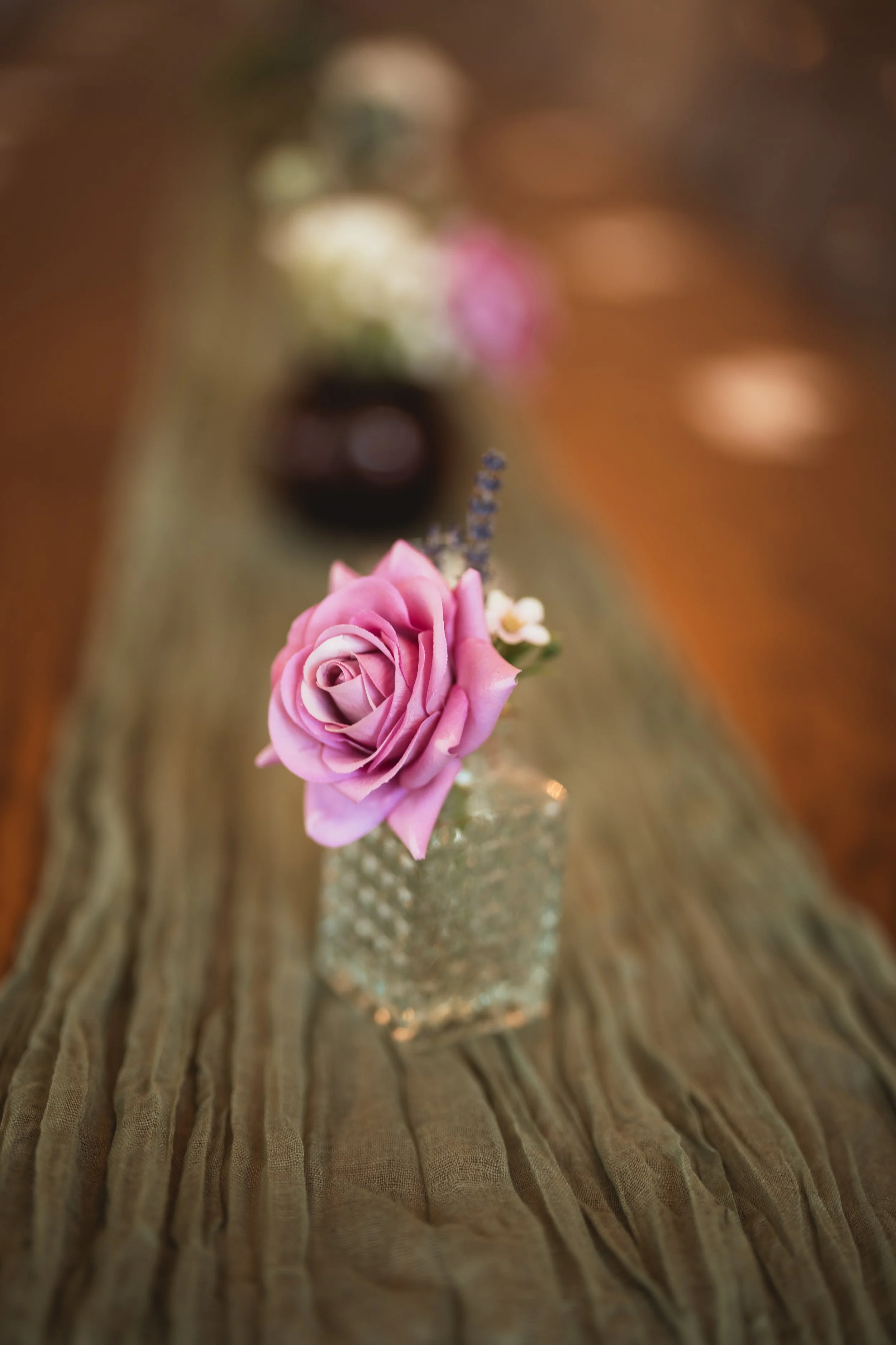 A wedding centerpiece in a budvase sits on top of a green cheesecloth runner available to couples whose wedding is planned by JayBird Weddings and Events