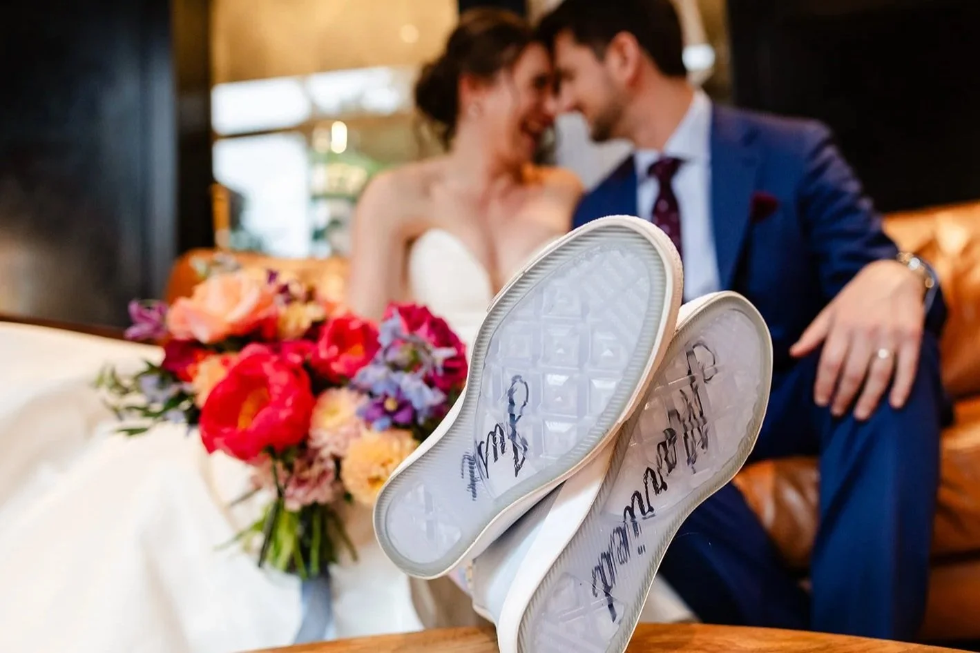 The camera focuses on the sole of a pair of sneakers that say "Just Married" as the bride and groom sit together in the background during their wedding planned by JayBird Weddings and Events.