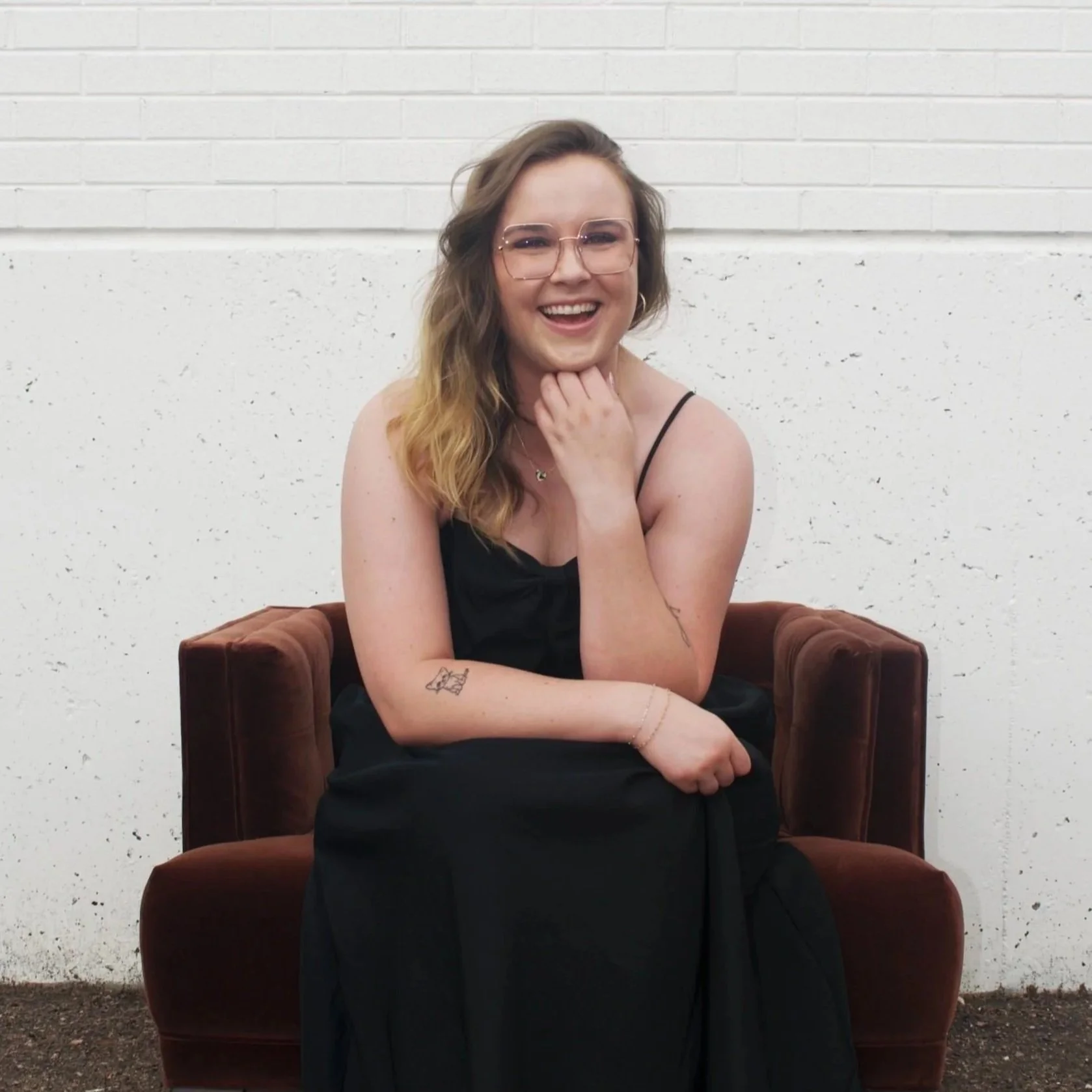 Moriah, the owner of JayBird Weddings and Events poses in a black dress seated on a dark brown armchair