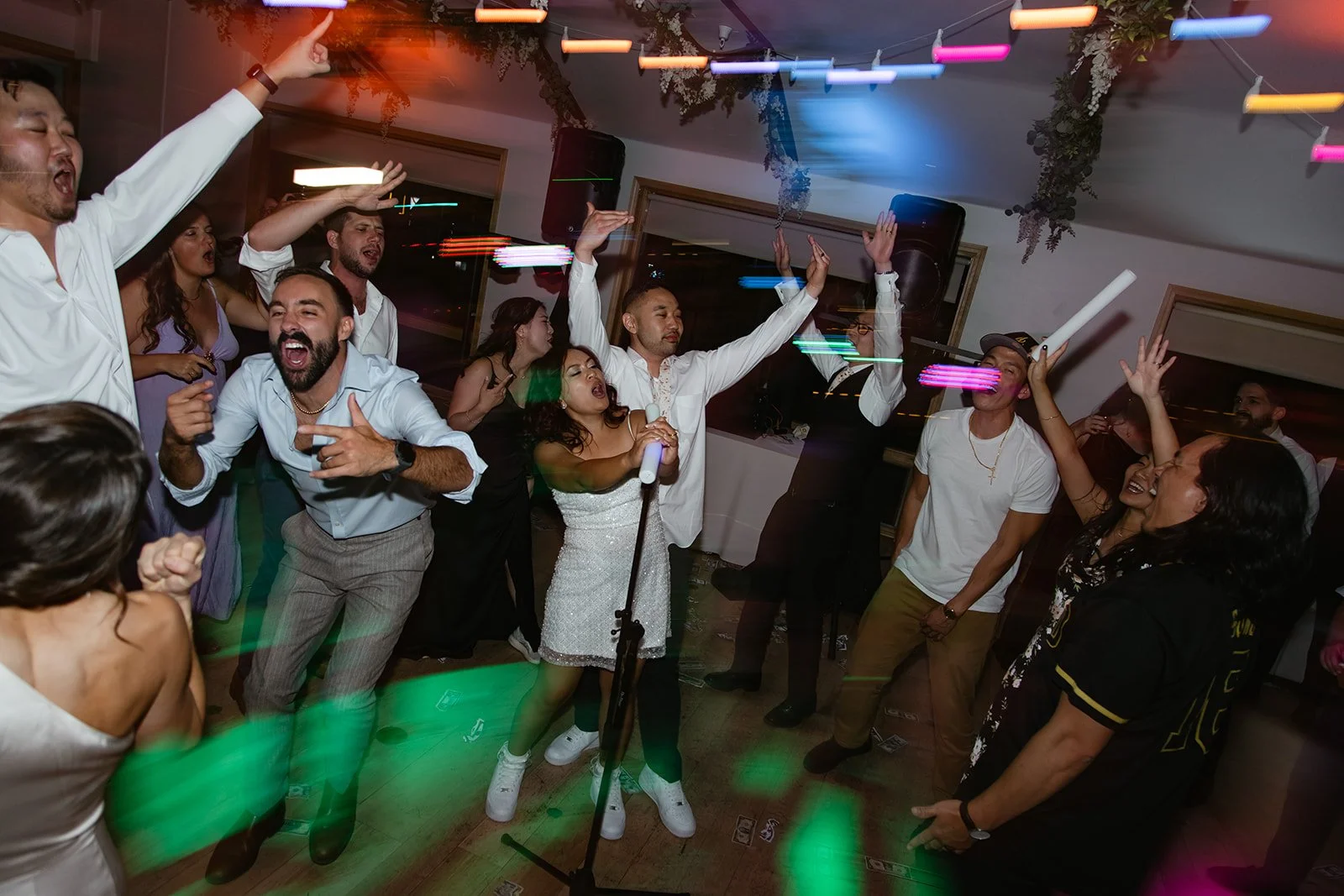 A bride sings into a foam LED light stick while dancing with her groom and her guests at her wedding planned by JayBird Weddings and Events
