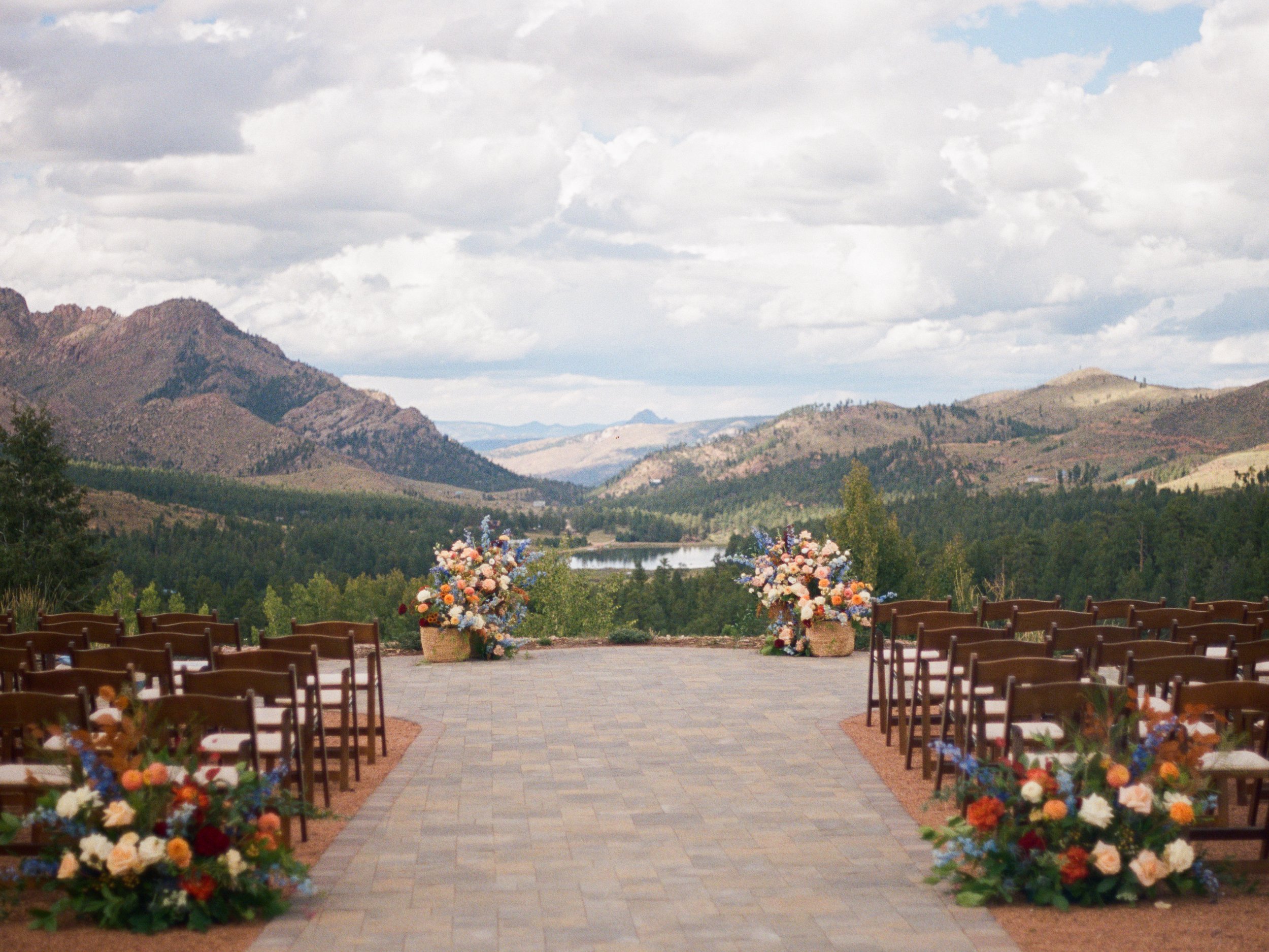 Chairs and florals line the aisle ahead of the altar, overlooking a stunning mountain range, prior to a wedding planned by JayBird Weddings and Events.