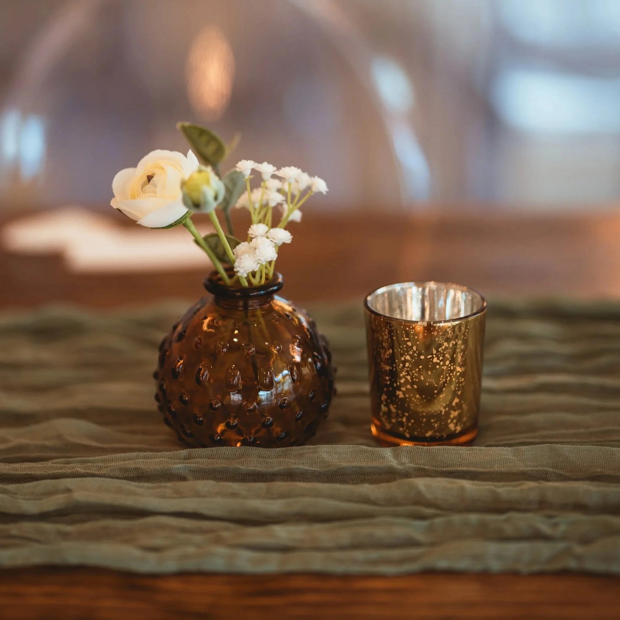 A rented gold candle votive next to a budvase of flowers at a wedding planned by JayBird Weddings and Events