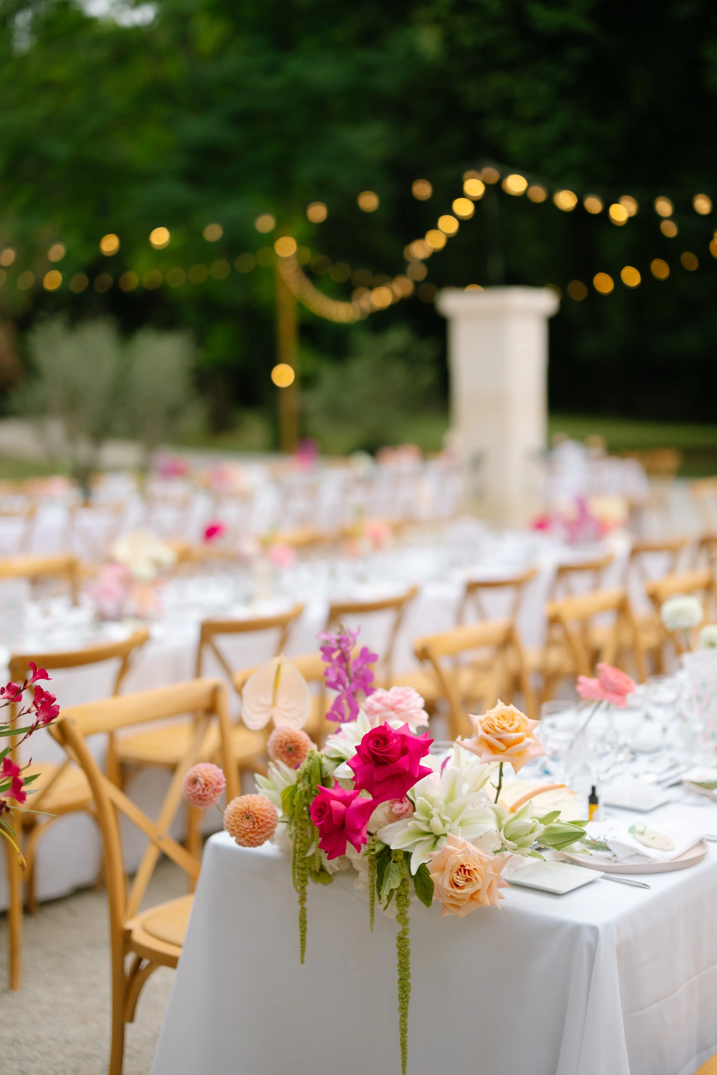 Un arrangement floral coloré avec des roses roses et crème, des fleurs blanches et des décorations suspendues dans un cadre extérieur lors d'un événement