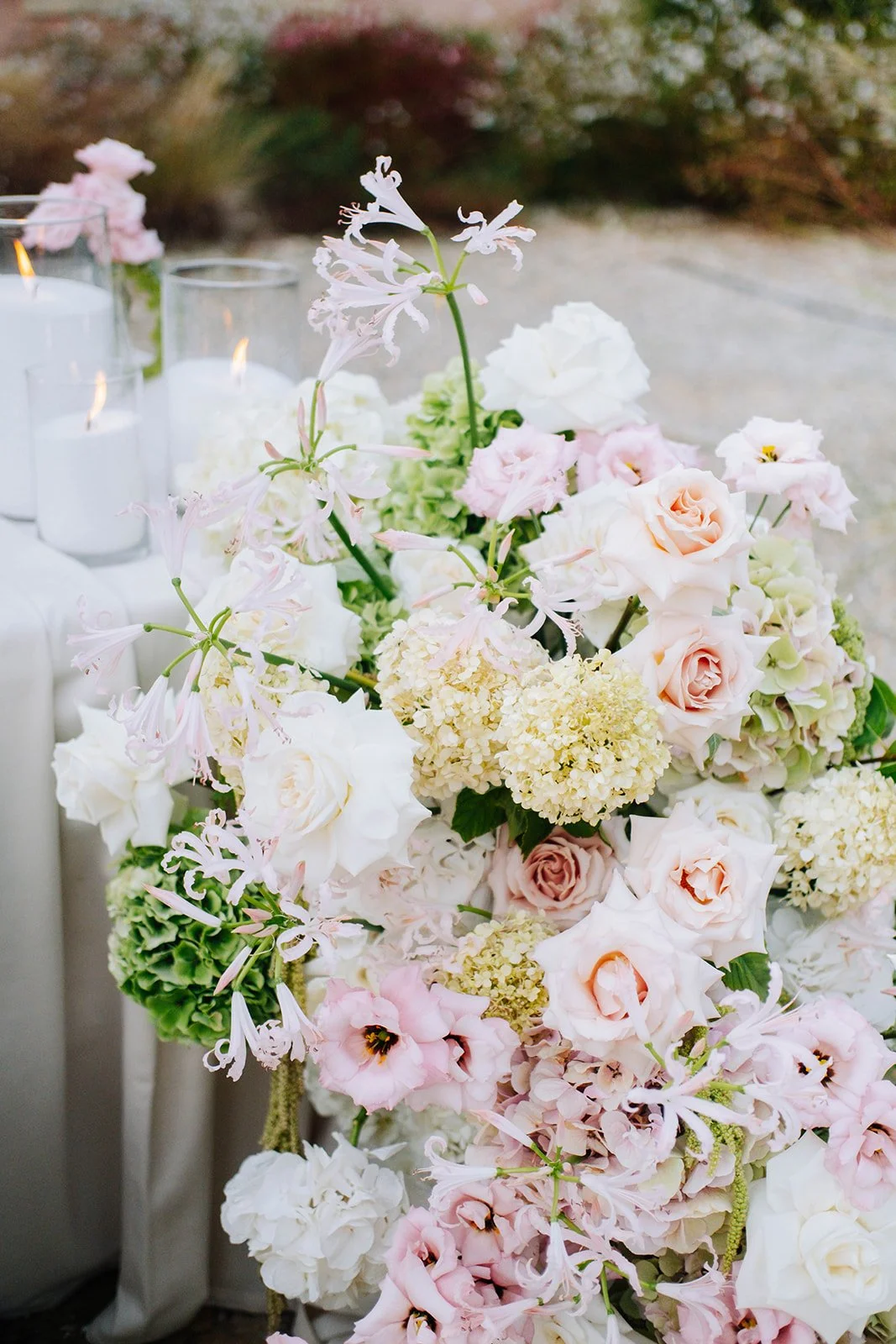 Bouquet de fleurs pastel avec des roses, hortensias, et autres fleurs, décoré avec des bougies dans des vases en verre.