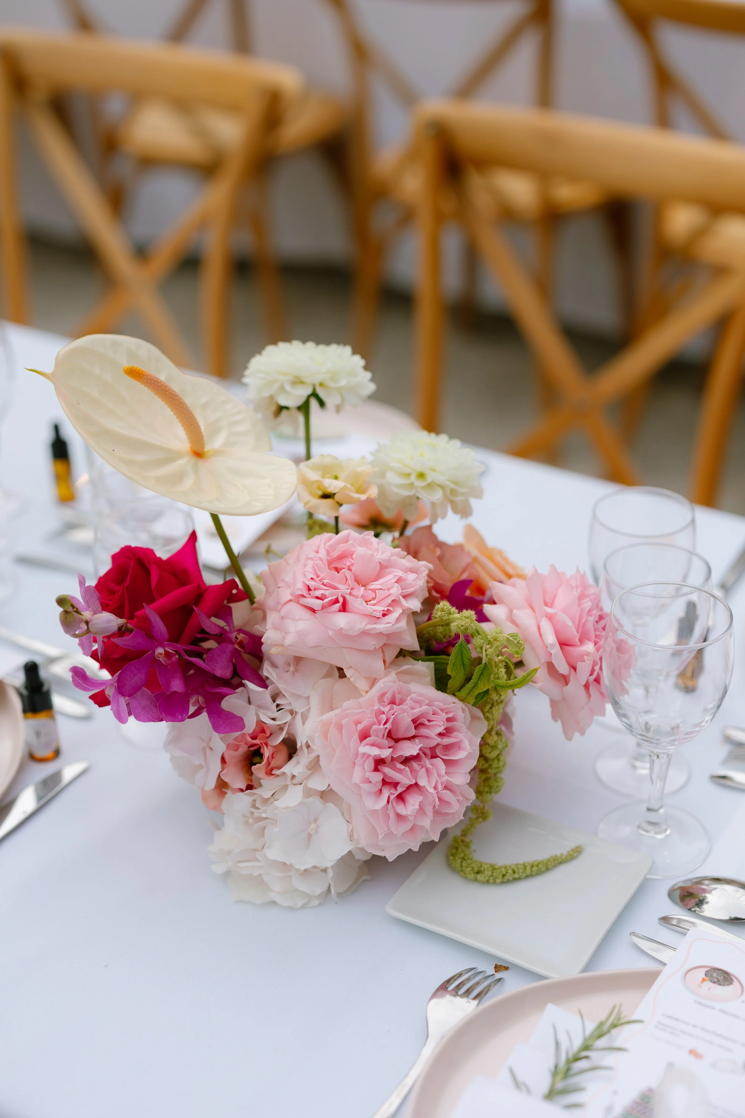 Une décoration florale composée de fleurs roses, blanches et violettes sur une table de réception. En arrière-plan, des chaises en bois sont visibles.