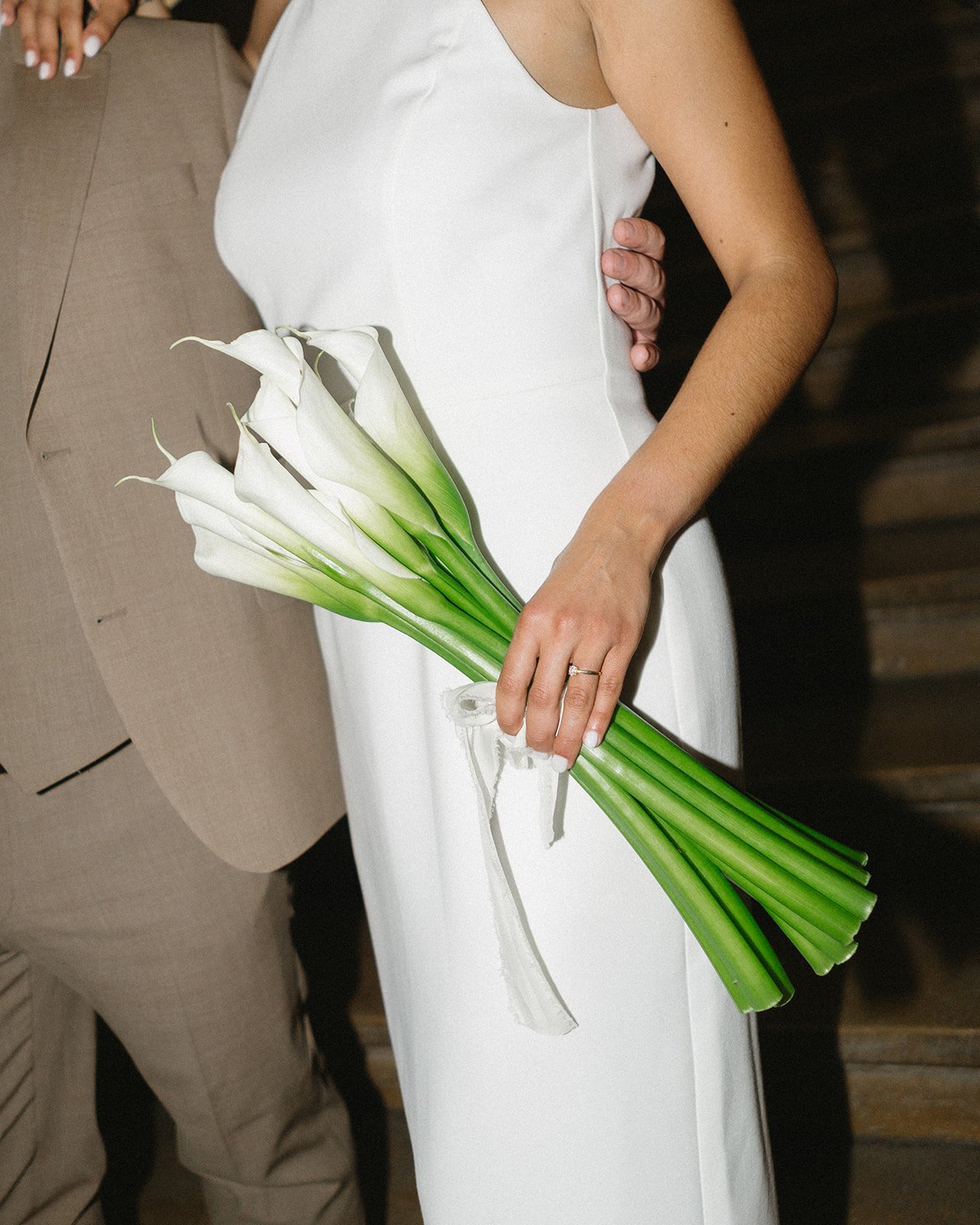 Une femme en robe blanche tient un bouquet de calla lilies blancs.