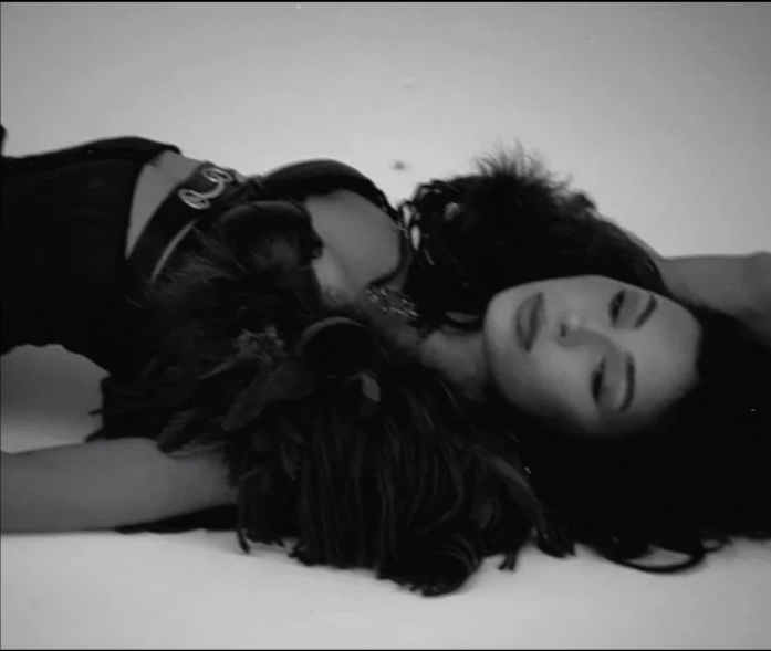 Black and white photo of a woman lying on a surface, wearing a dark outfit with fur details.