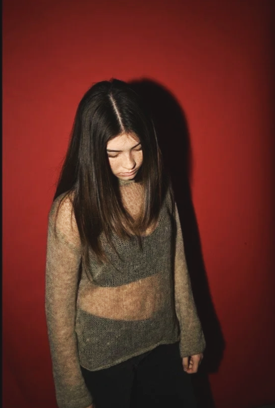 Person with long hair looking down against a red background