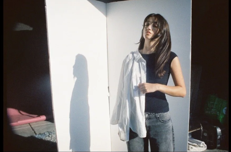 Person holding a white shirt while standing in front of a white board, casting a shadow.