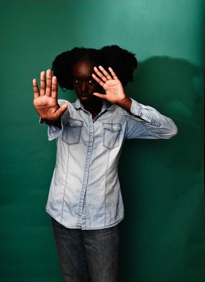 Person in denim shirt with hands raised against green background