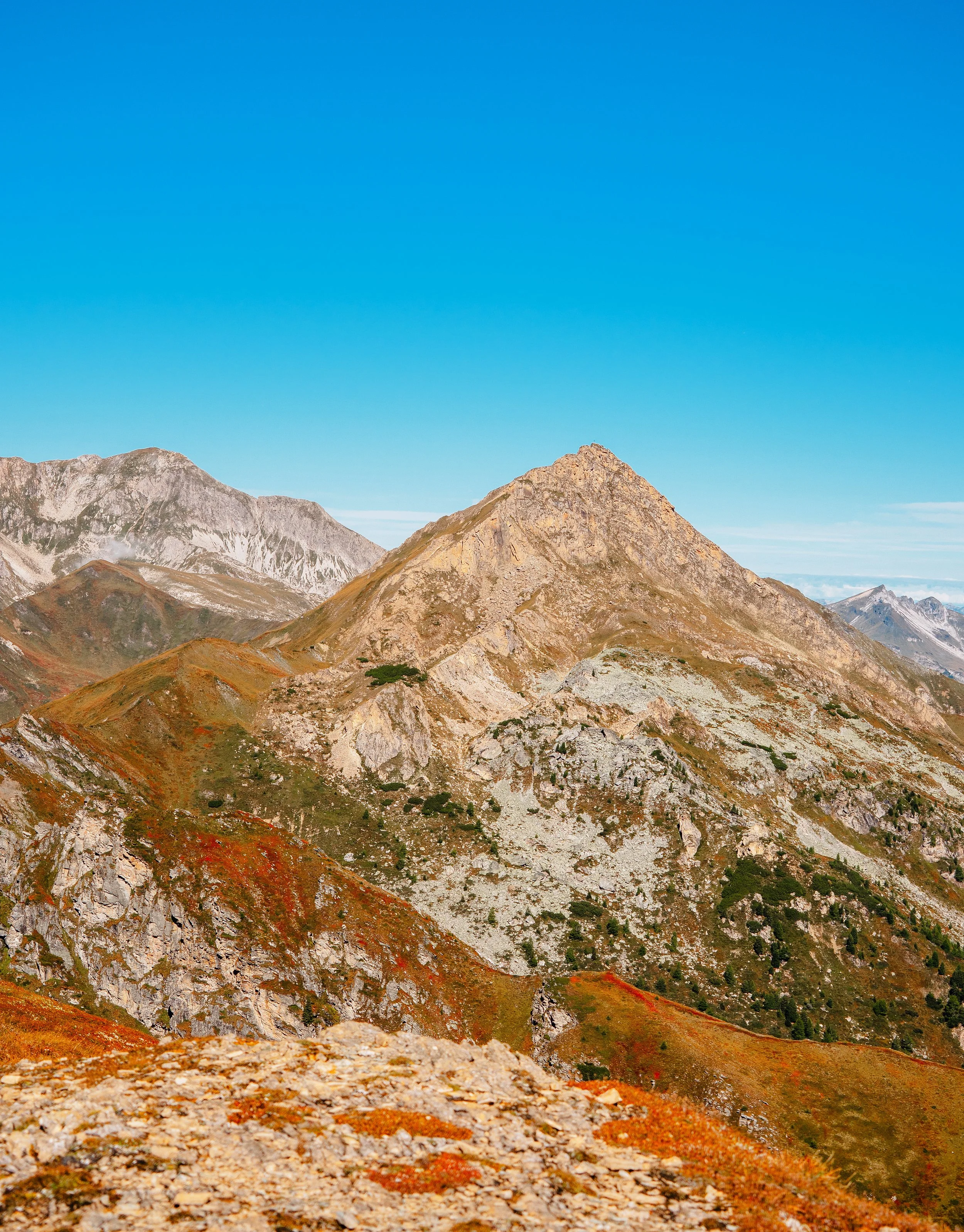 Berglandschaft mit orange-braunen und grünen Hügeln unter klarem blauen Himmel.