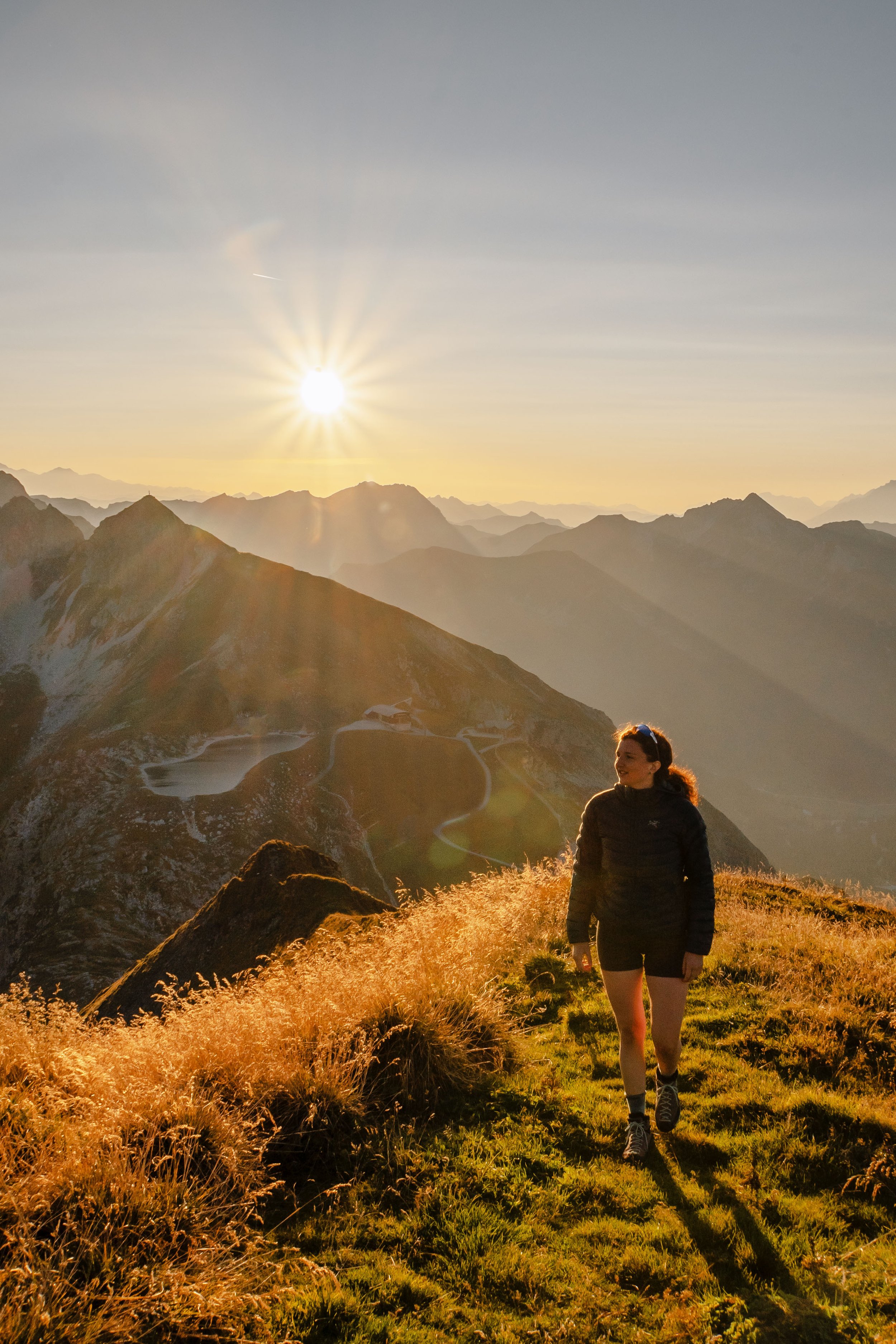 Eine Frau wandert in den Bergen bei Sonnenuntergang mit Blick auf Täler und Bergseen.