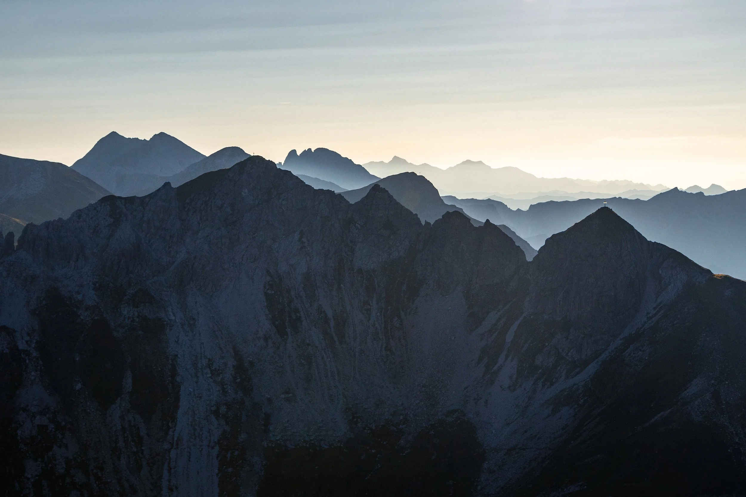 Berglandschaft bei Sonnenaufgang mit mehreren Gipfeln in unterschiedlichen Dämmerungsstufen.