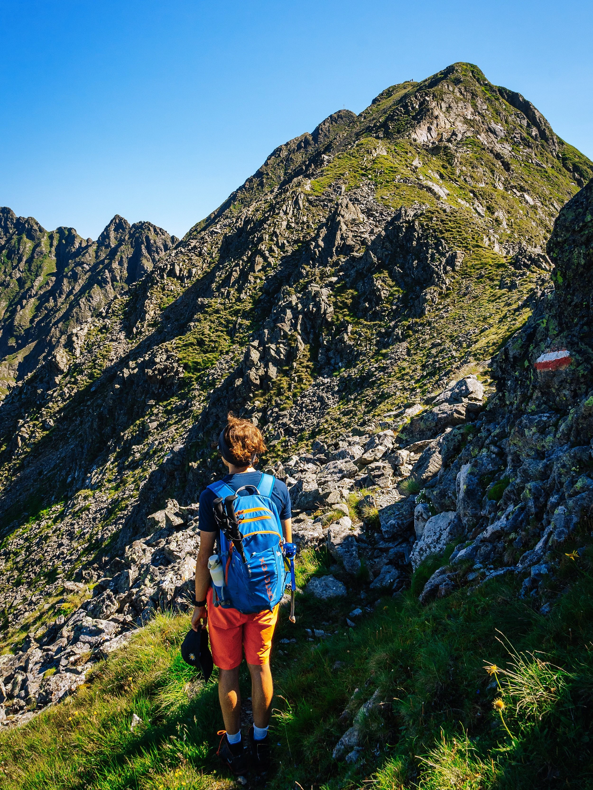Junge Person beim Wandern in den Bergen mit Rucksack und Blick auf die Gipfel bei sonnigem Himmel.