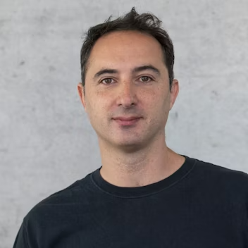 Lorenzo Zanasi, a man with short dark hair wearing a dark t-shirt, standing against a plain light grey background.
