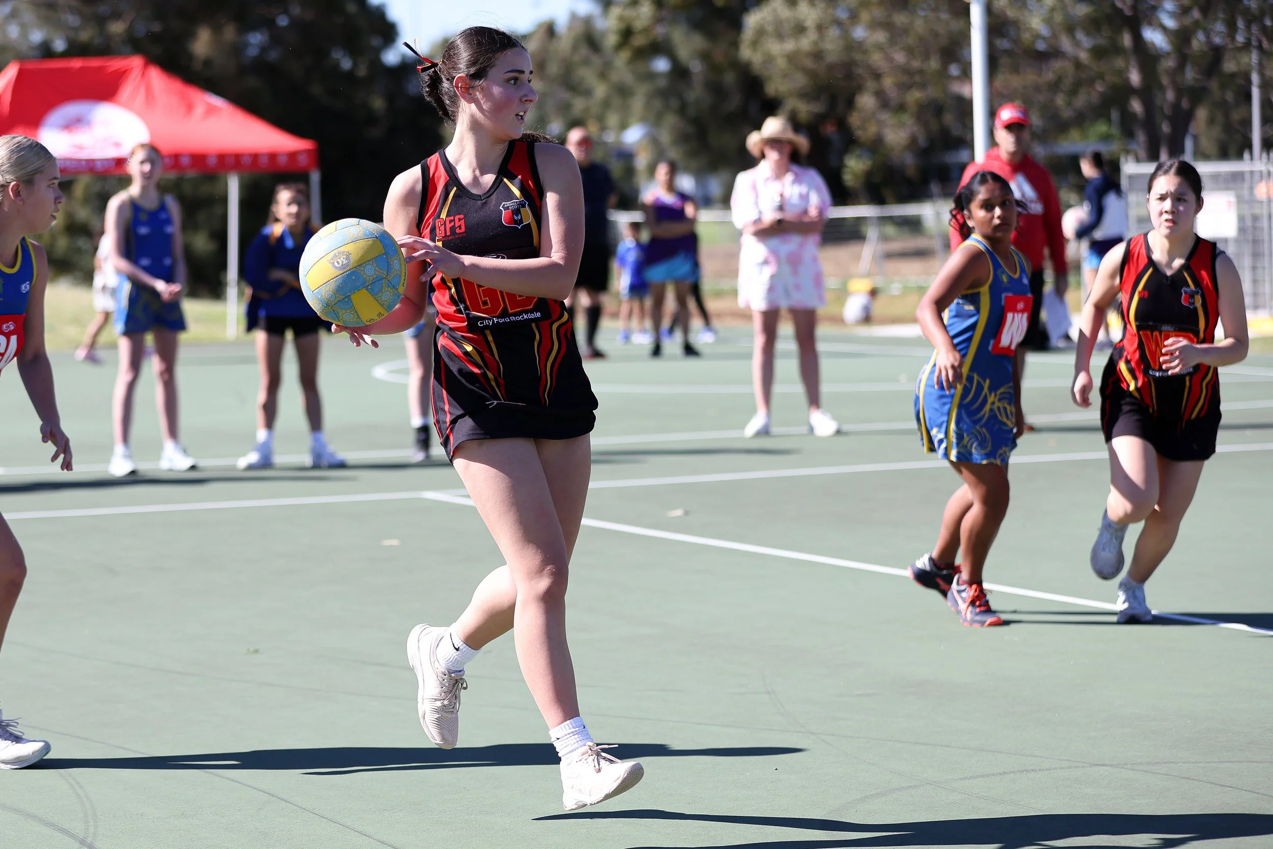 Girls playing a netball game outdoors on a court.