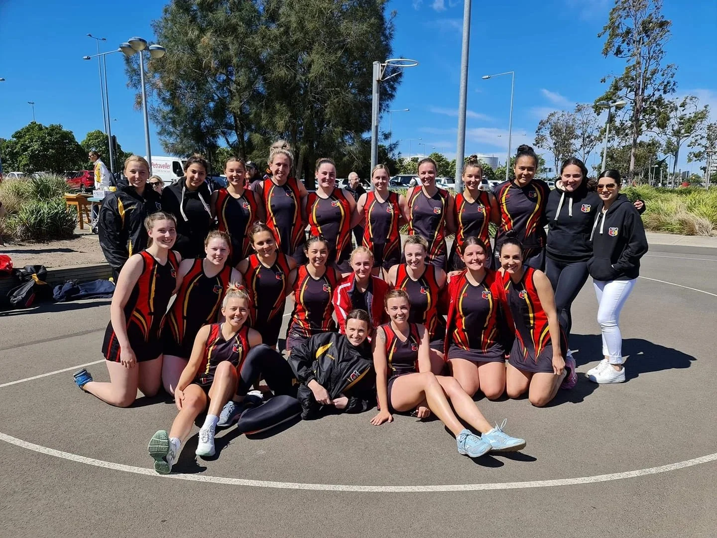 Group of female athletes in netball uniforms posing outdoors on a court.