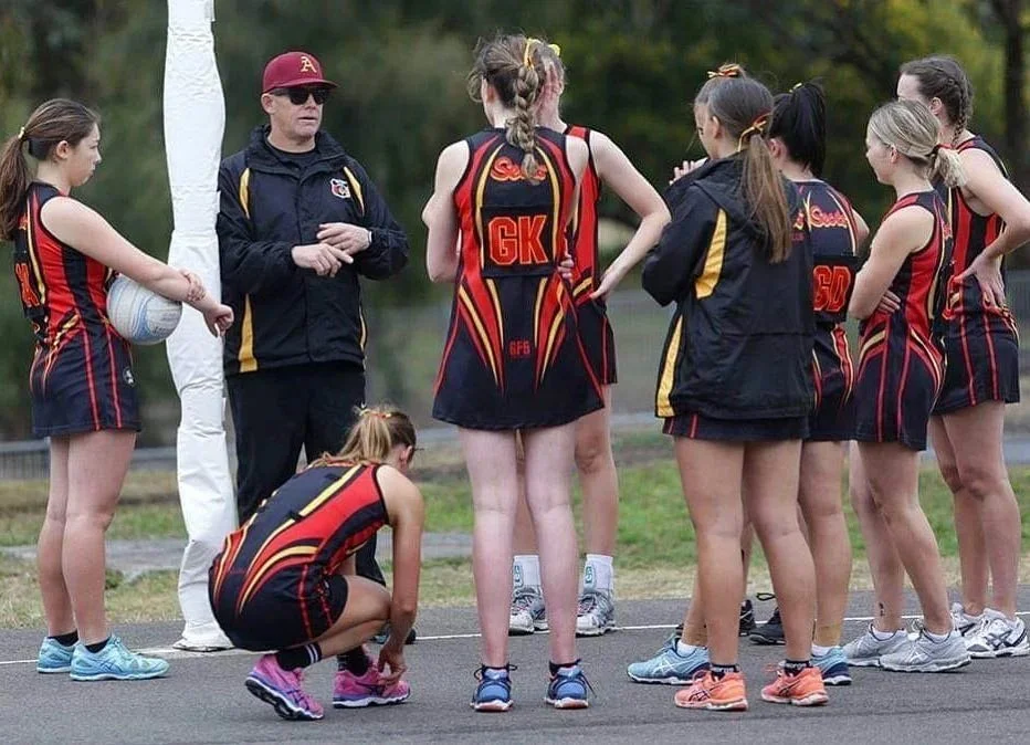 Netball team huddle with coach outdoors