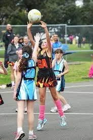 Young girls playing netball outdoors on a court with one girl jumping to catch the ball.