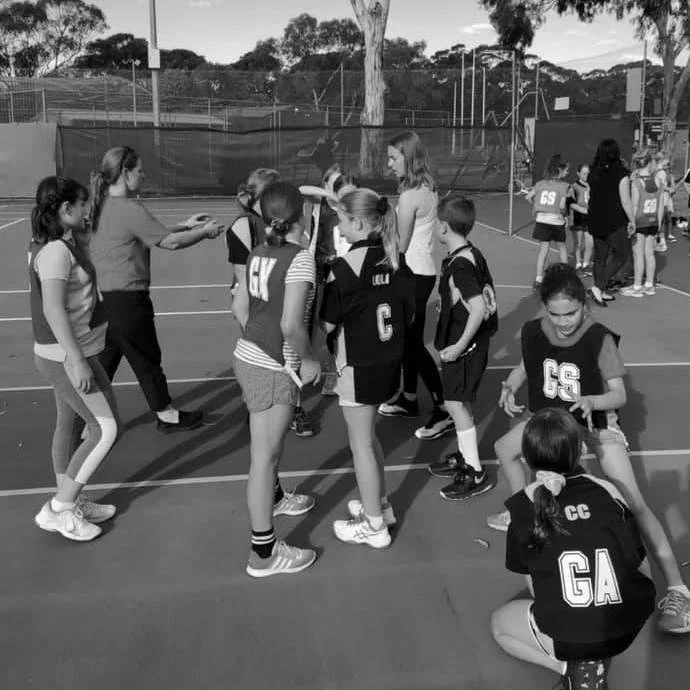 Children in sports uniforms on an outdoor court receiving instructions