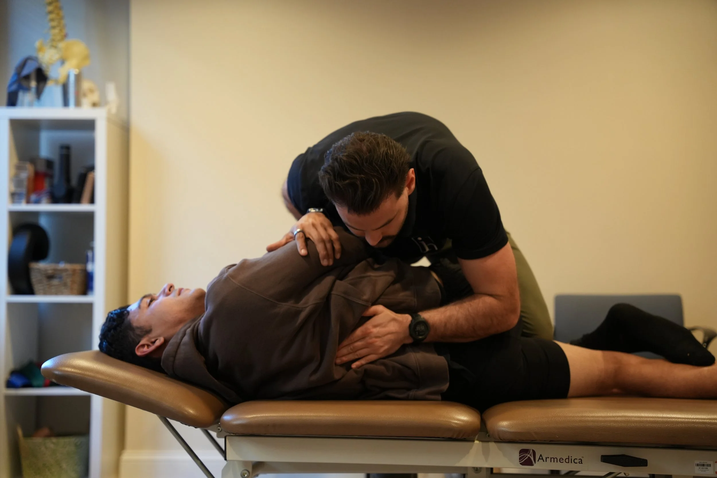 Two people shaking hands, one sitting and one standing, with a plain background.