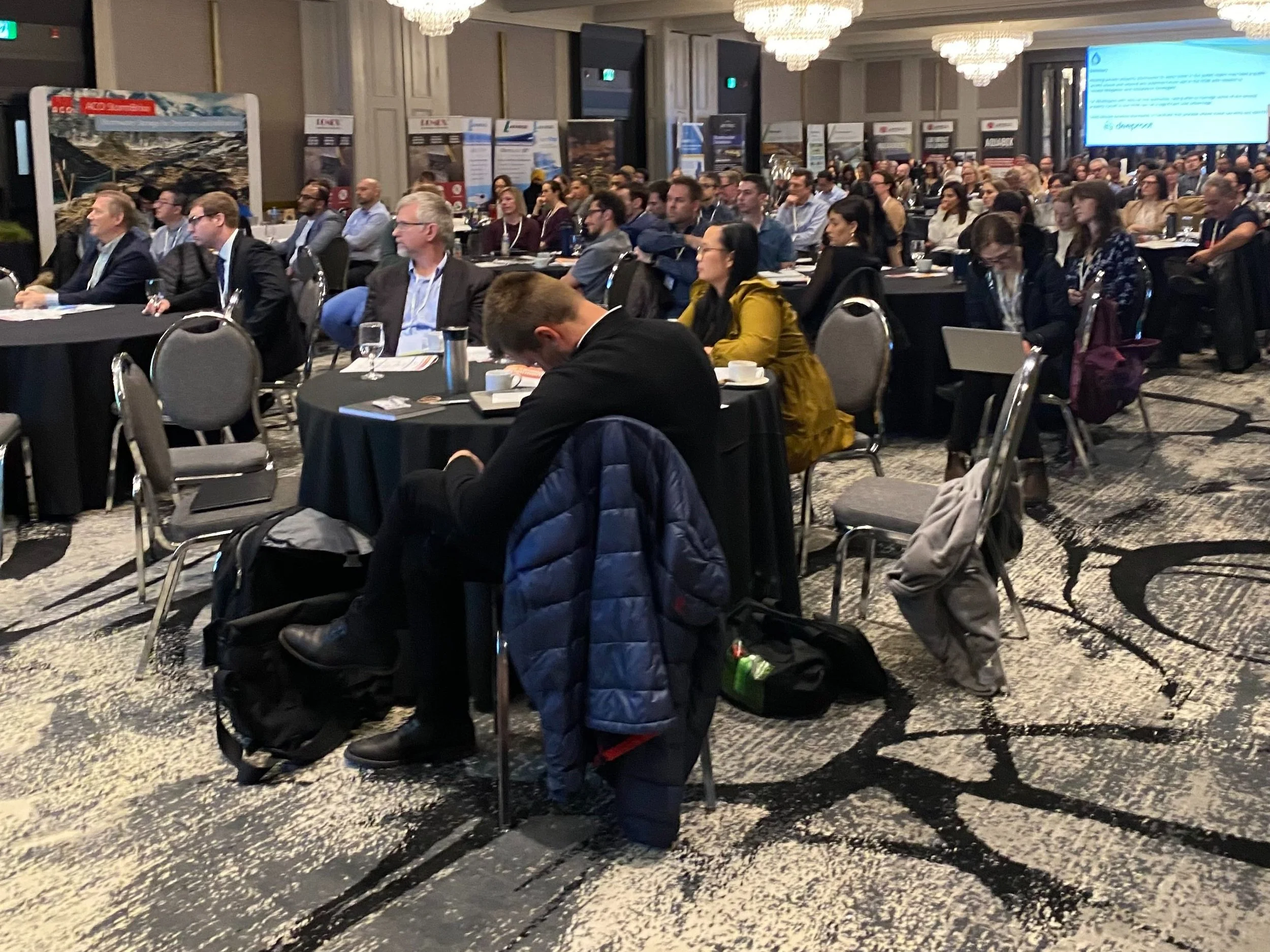 a room of conference attendees watching a presentation with a perimeter of exhibitor displays in the distance