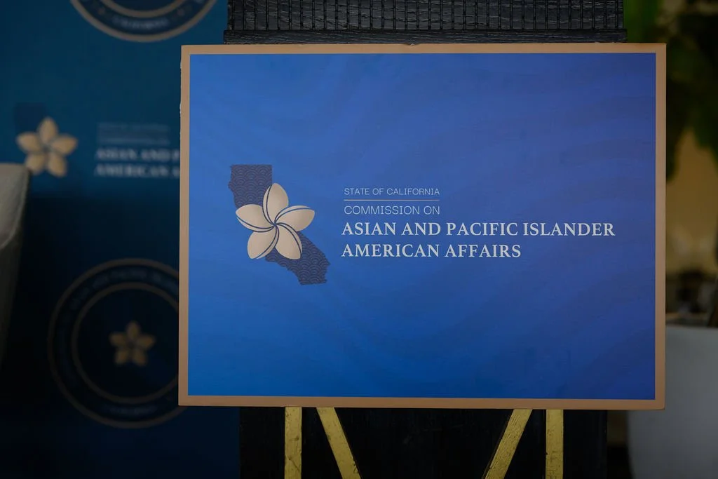 A sign for the California Commission on Asian and Pacific Islander American Affairs with a blue background, white flower, and a California map outline.