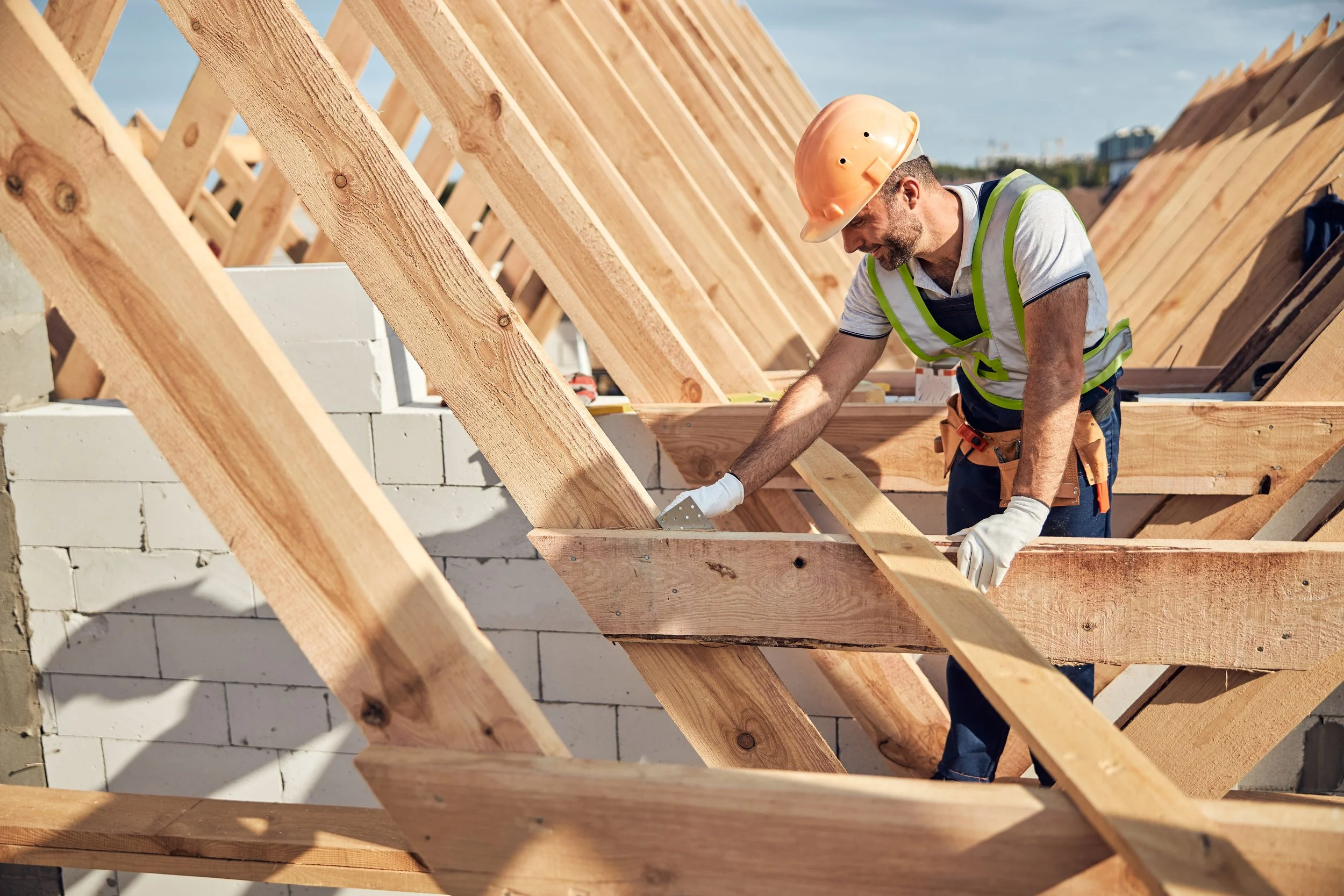 Homme en casque et gilet de sécurité travaillant sur une charpente en bois.