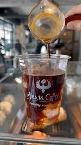 A hand pouring a light-colored espresso into a glass cup of iced coffee at a cafe.