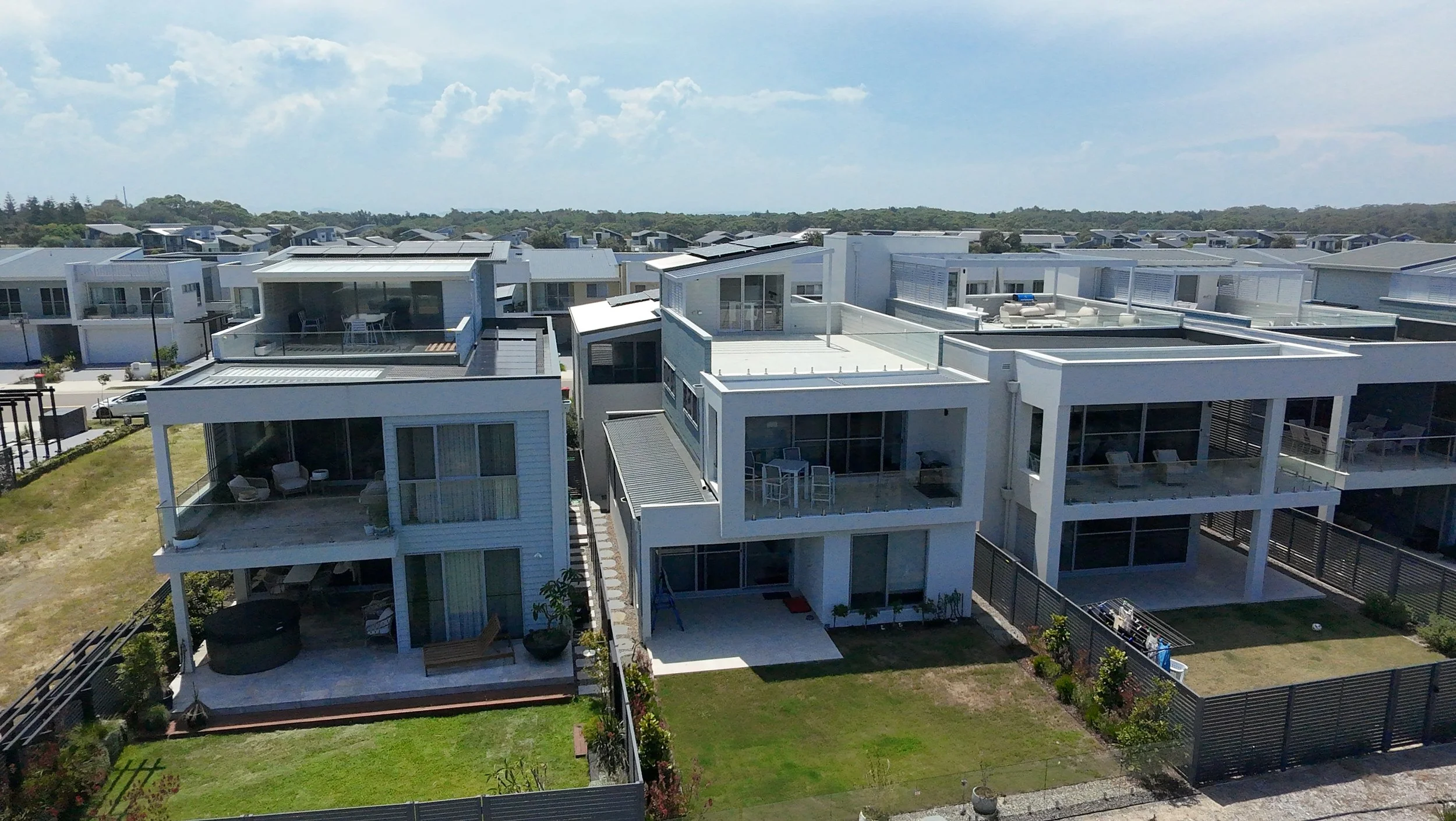 Aerial view of modern white homes with flat roofs and balconies in a residential neighborhood.