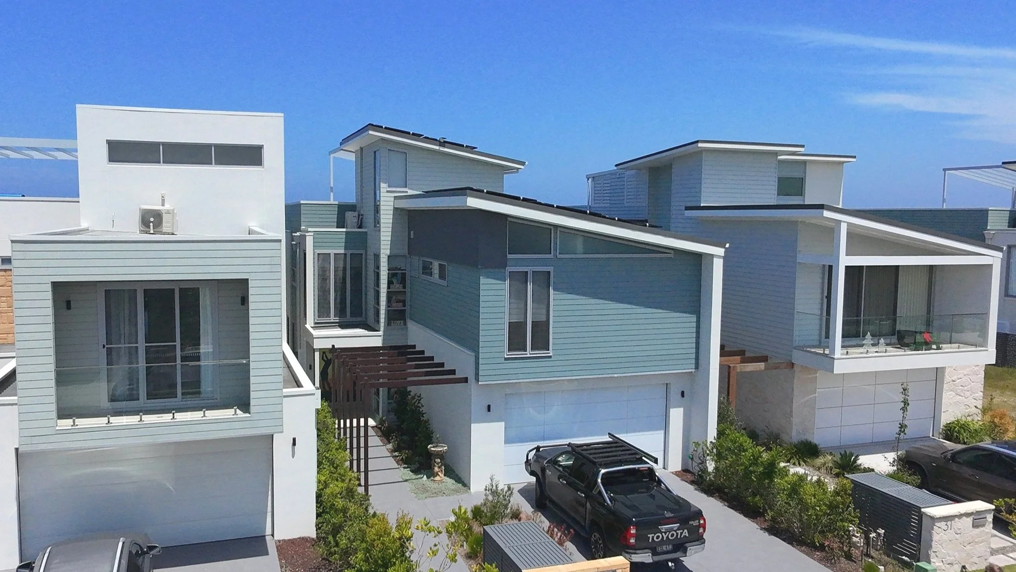 Contemporary two-story houses with garages and landscaped driveways under a clear blue sky.
