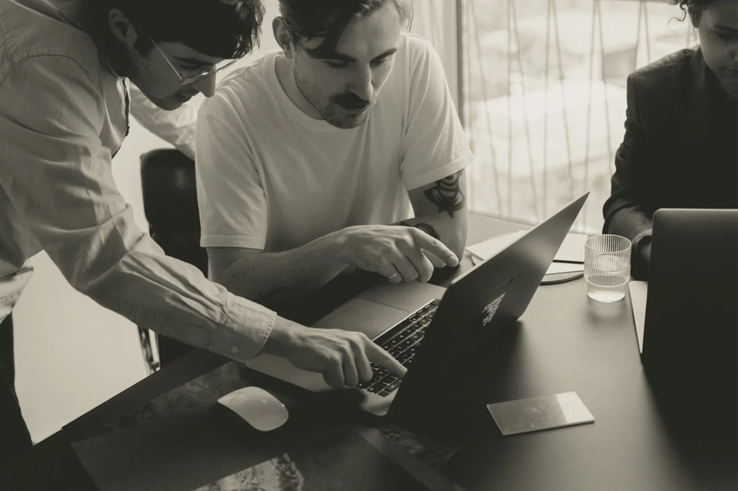 Three colleagues collaborating around a laptop in a bright office.