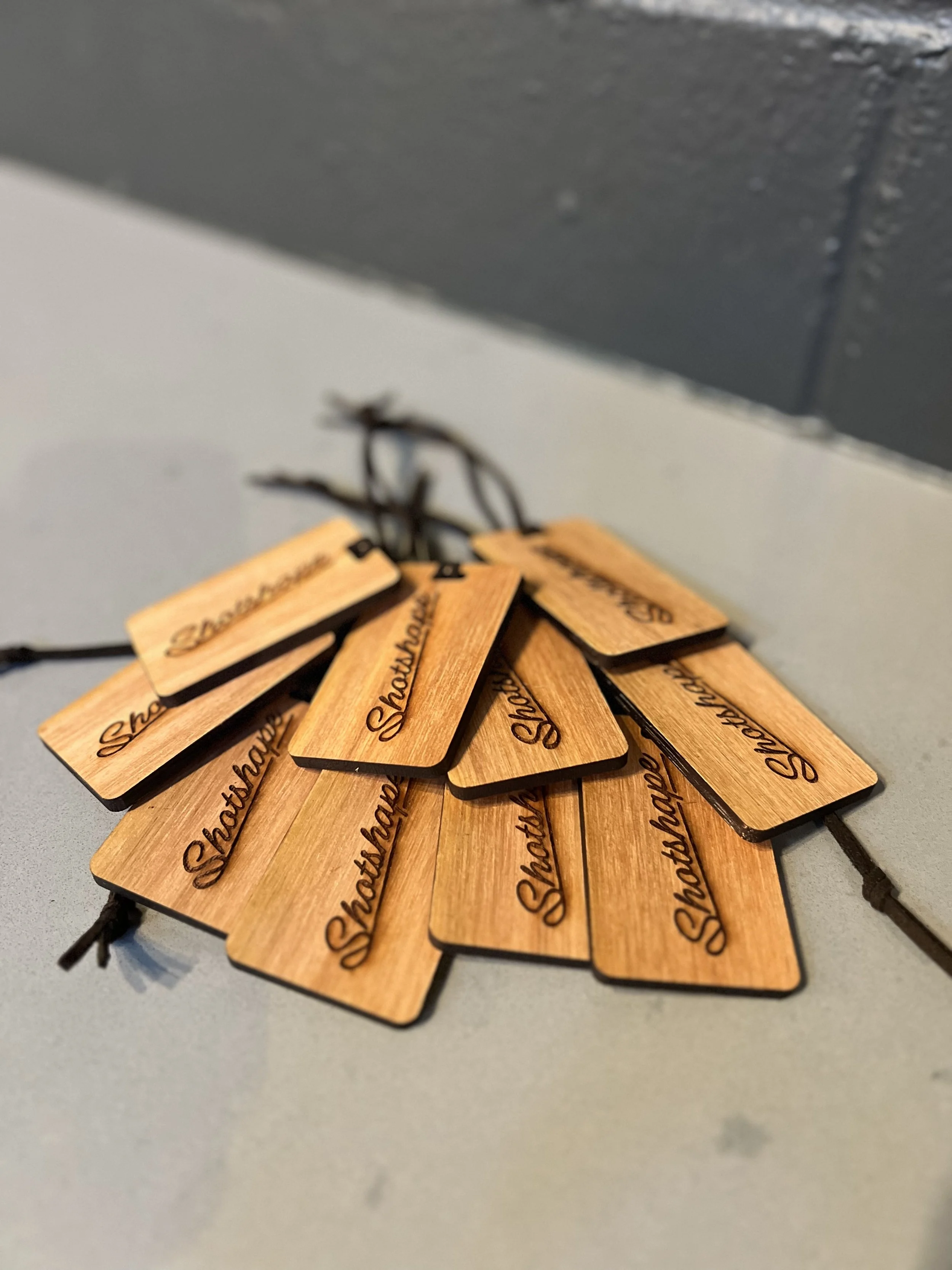 A pile of wooden golf bag tags with the word 'Shotshape' engraved on them, tied with black strings.