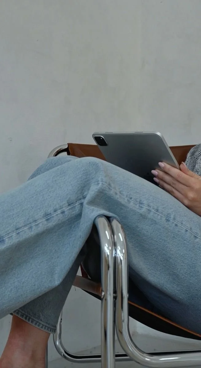 Person sitting with tablet in lap, wearing jeans and sitting on a modern chair.