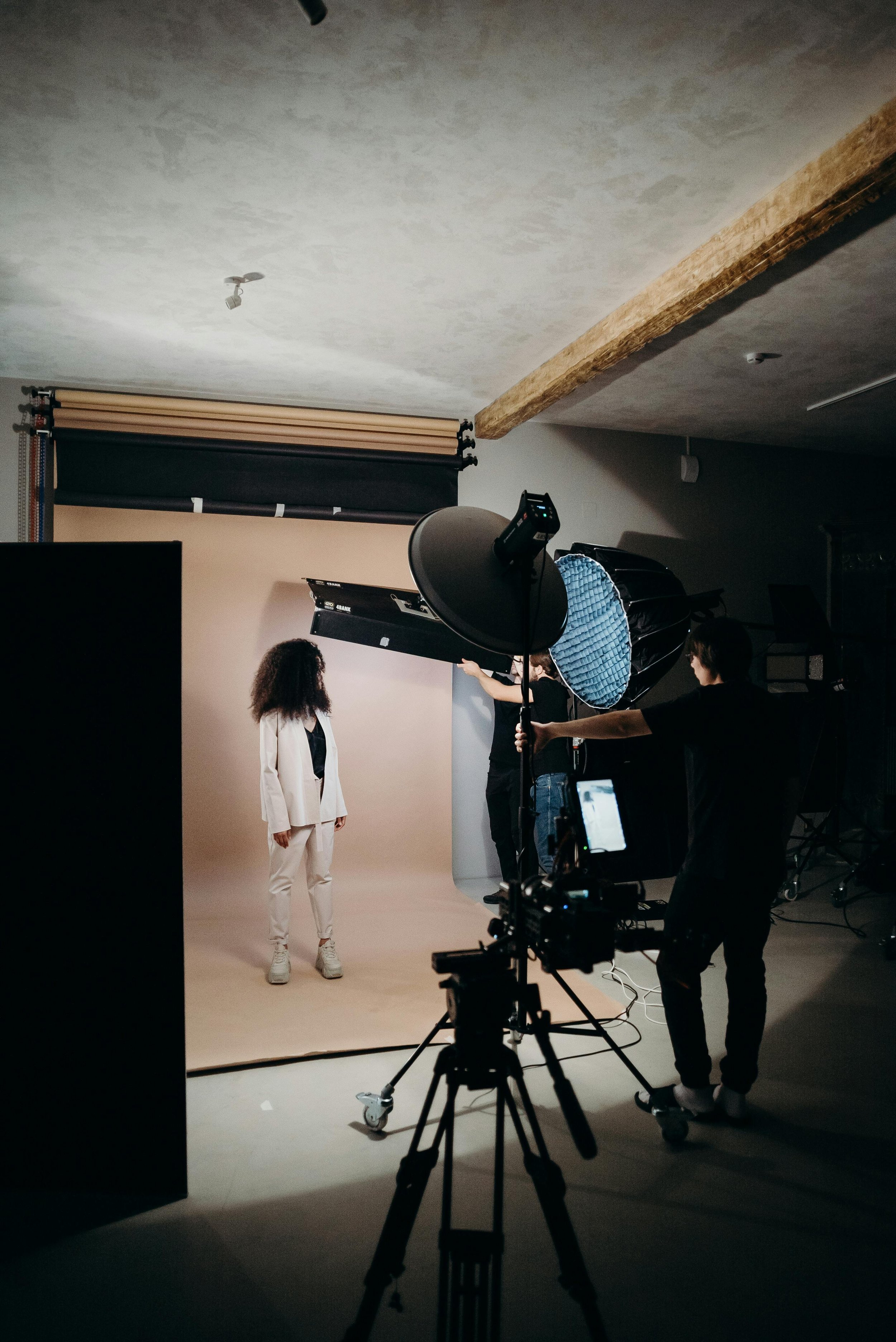 Photography studio setup with a model in a white outfit, lighting equipment, and photographers adjusting lights.